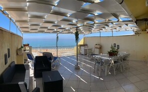 Un espacio al aire libre techado con vista al mar, una mesa con sillas y un sofá.