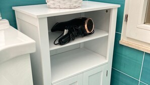 A bathroom with a white vanity, a white shelf with a woven basket, and a black hairdryer. - Terrace overlooking the sea (Scoglitti)