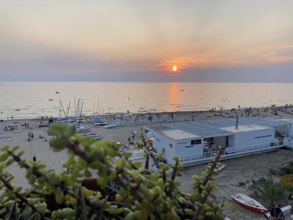 Una playa con barcos, sombrillas y un edificio con un letrero.