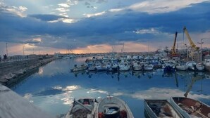 A marina with numerous boats docked, a crane, and a calm water body reflecting the sky. - Terrace overlooking the sea (Scoglitti)