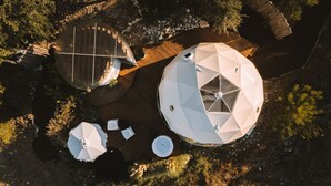 Vista aérea de una propiedad con varias estructuras en forma de cúpula, una terraza de madera y vegetación circundante.