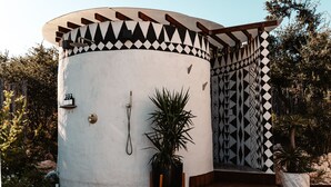 Una estructura cilíndrica con un exterior de diseño geométrico, un banco de madera y una planta en maceta.