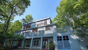 A two-story wooden house with a balcony, surrounded by trees. - Designer Lakefront Retreat with Panoramic Sunset Views (Harrison)