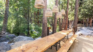 Puinen piknikpöytä metsäisellä alueella, jonka yläpuolella roikkuu koristeellisia rottinkilyhtyjä.