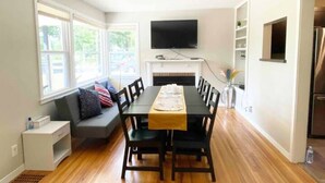 A dining area with a long table, chairs, a TV mounted above, and a fireplace. - Sunny Retreat Haven (Minneapolis)