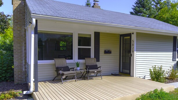 A single-story house with a covered porch, two chairs, a small table, and a potted plant. - Sunny Retreat Haven (Minneapolis)