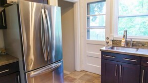 A kitchen with a stainless steel refrigerator, dark wooden cabinets, a window with a view of greenery, and a sink with a faucet. - Sunny Retreat Haven (Minneapolis)