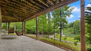A covered outdoor area with a swing, gravel flooring, and a view of a lake and forest. - Large Cabin Located on Deer Water Lake (Rogers)