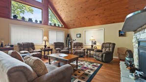 A spacious living room with high ceilings, wooden beams, and large windows. There are multiple leather armchairs, a wooden coffee table, and a fireplace. - Large Cabin Located on Deer Water Lake (Rogers)