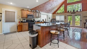 A spacious kitchen with a large island, wooden cabinets, and a high ceiling with exposed beams. - Large Cabin Located on Deer Water Lake (Rogers)
