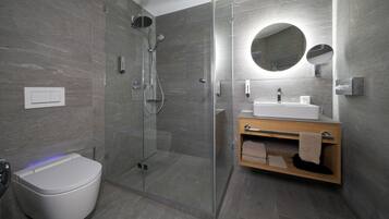 Ein modernes Badezimmer mit einer Duschkabine, einer weißen Toilette und einem Holzausleger mit Spiegel.