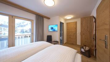 A hotel room with two beds, a TV, a wooden wardrobe, and a balcony with a mountain view.