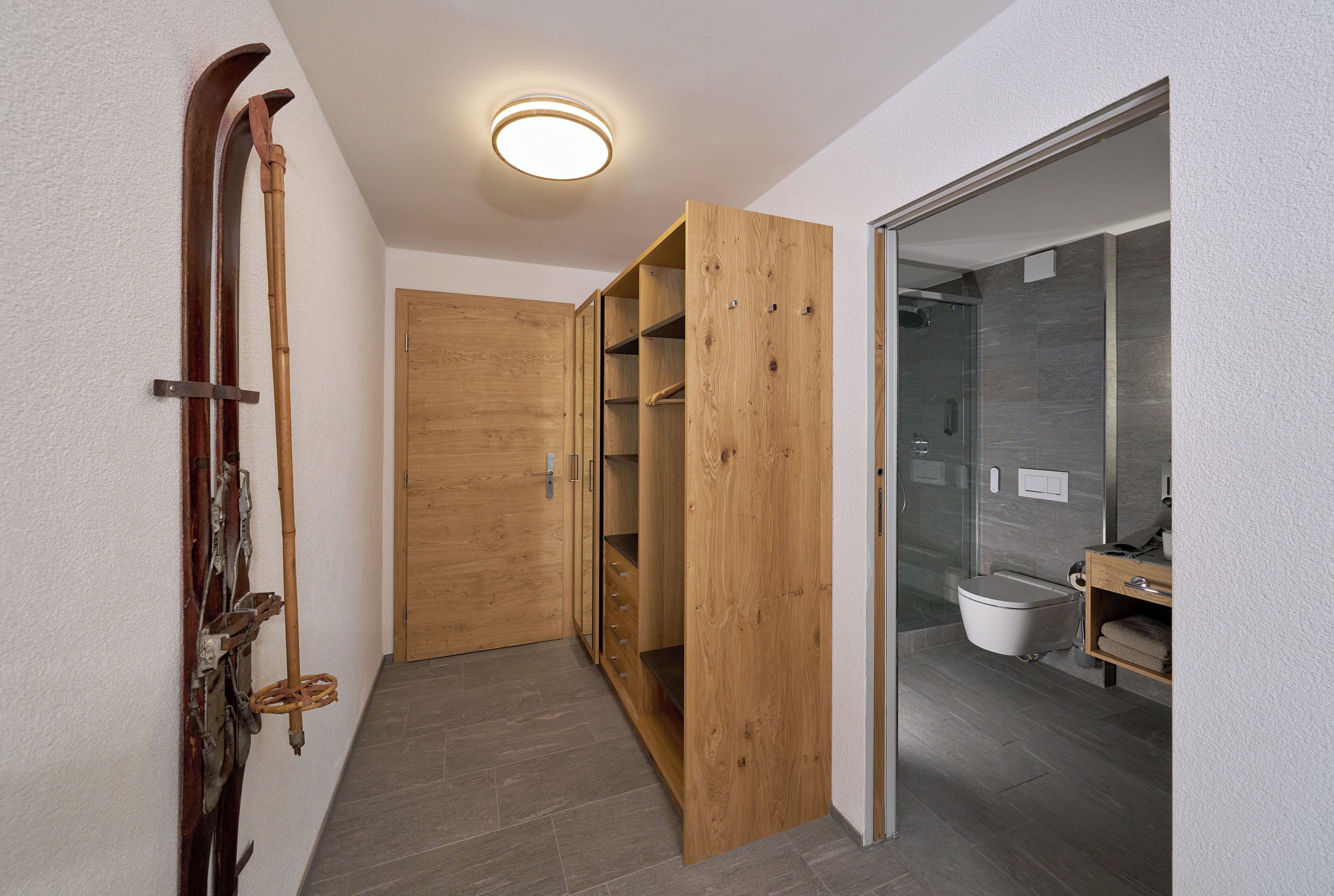Un couloir avec des portes en bois, un espace douche et des toilettes.
