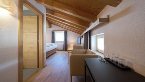 A modern hotel room with a wooden ceiling, a bed, a sofa, a small table with glasses, and a window.