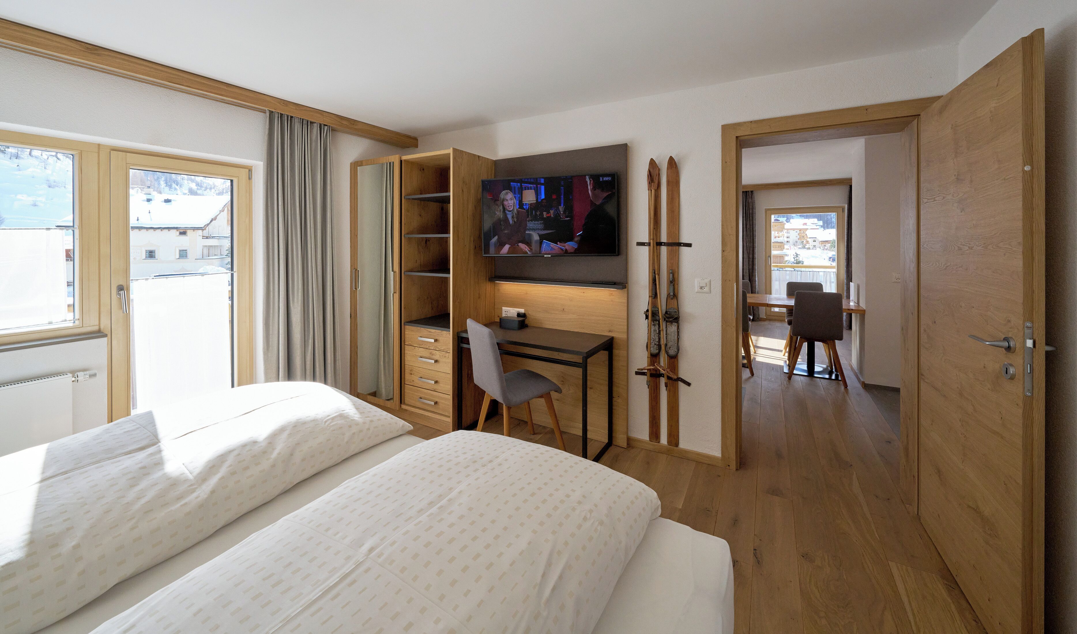 A hotel room with a bed, a desk with a chair, a TV, and a ski rack.