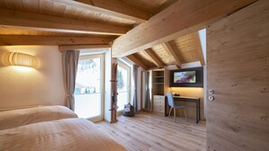 A room with wooden beams, a bed, a desk, a chair, a TV, and a window with curtains.