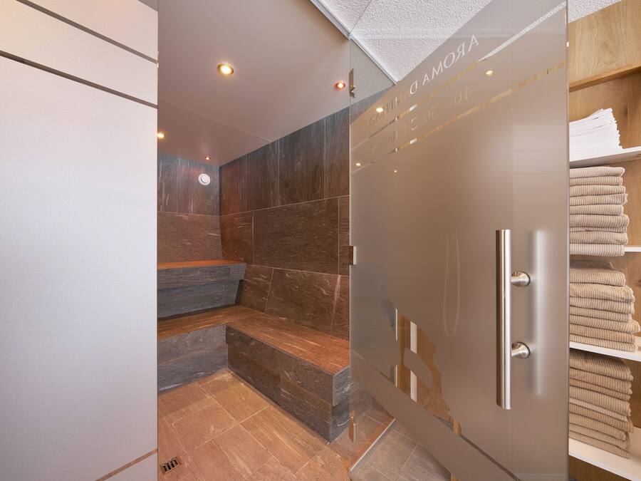 A modern bathroom with a glass shower enclosure, a marble-tiled wall, and a wooden shelf with towels.