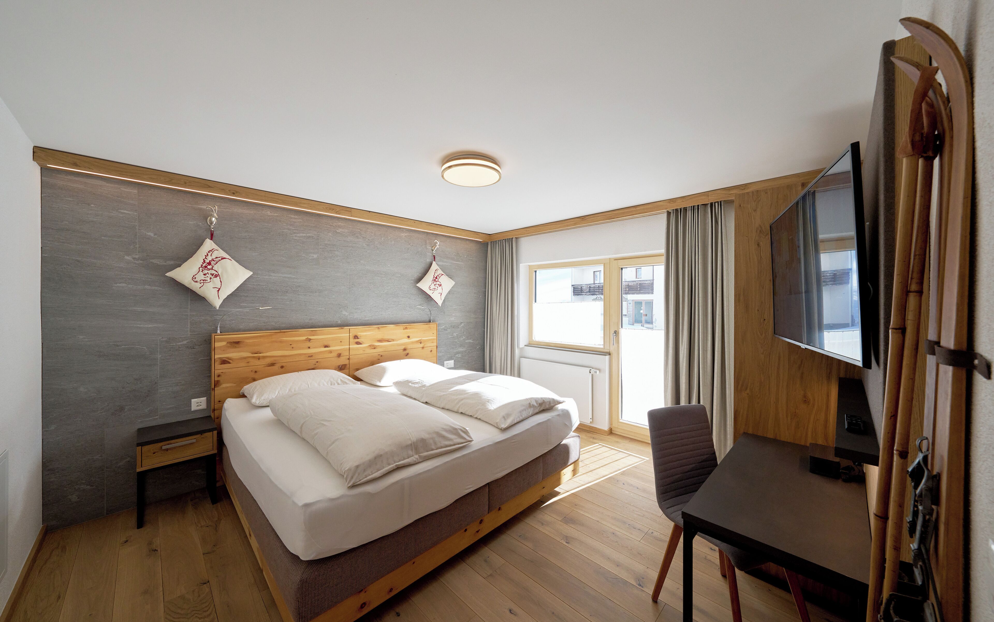 Une chambre d’hôtel avec un lit en bois, un bureau, une chaise, une télévision et une fenêtre avec des rideaux.