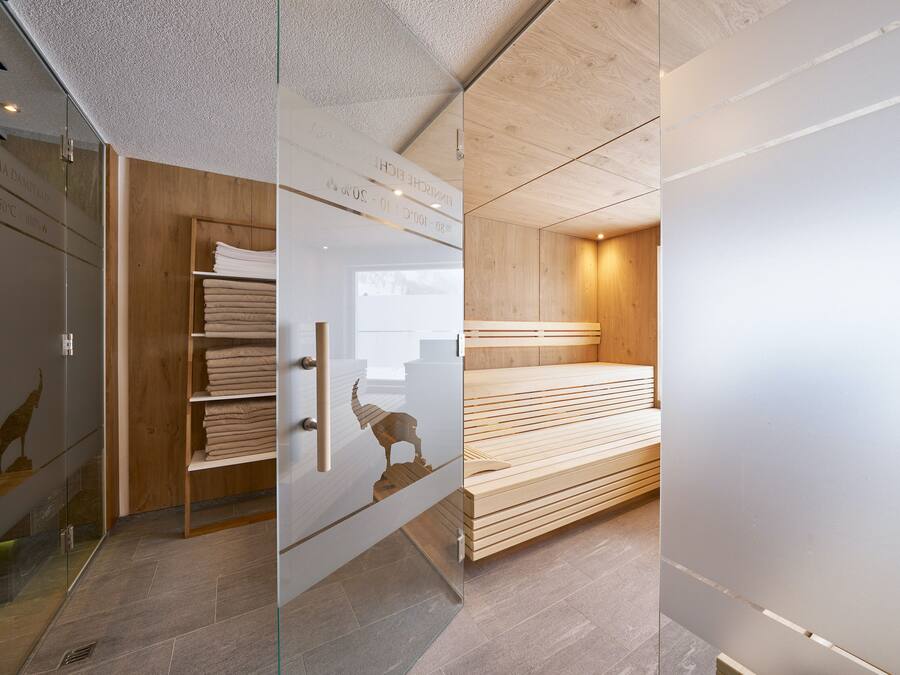 A modern bathroom with a glass shower enclosure, wooden shelving with towels, and a wooden bench.