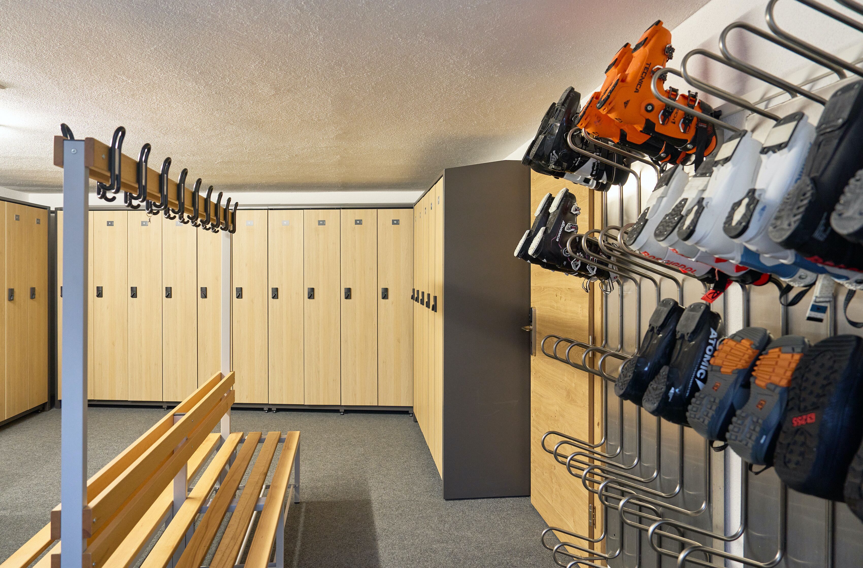 A locker room with wooden lockers, a bench, and a shoe rack with various types of footwear.