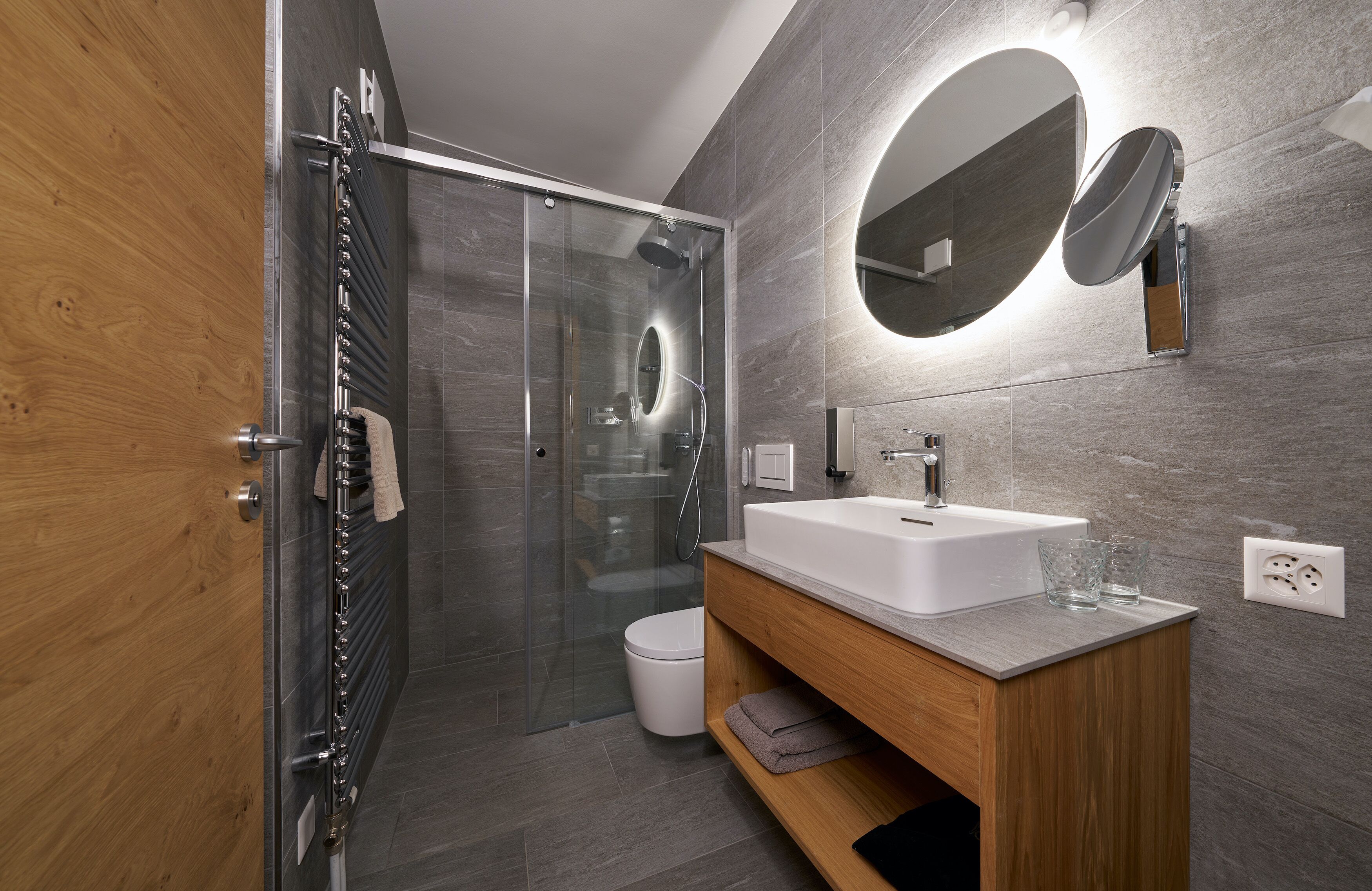 A modern bathroom with a glass-enclosed shower, a white sink, and a wooden vanity.
