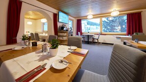 A dining area with a wooden table set for two, a potted plant, and a television screen displaying a Google search.