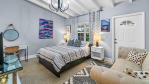 A bedroom with a bed, bedside tables, a chair, a sofa, a chandelier, and a door. - Experience Tranquility at The Sago: Newly Remodeled Studio with Private Patio (Delray Beach)