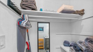 A laundry room with a mirror, shelves with folded towels, and a broom leaning against the wall. - Experience Tranquility at The Sago: Newly Remodeled Studio with Private Patio (Delray Beach)