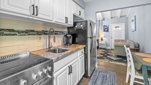 A modern kitchen with white cabinets, a stainless steel stove, and a refrigerator. - Experience Tranquility at The Sago: Newly Remodeled Studio with Private Patio (Delray Beach)
