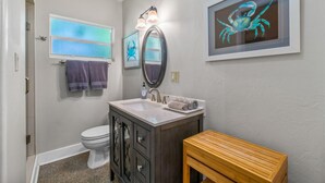 A bathroom with a toilet, vanity with a mirror, framed artwork, and a wooden bench. - Experience Tranquility at The Sago: Newly Remodeled Studio with Private Patio (Delray Beach)