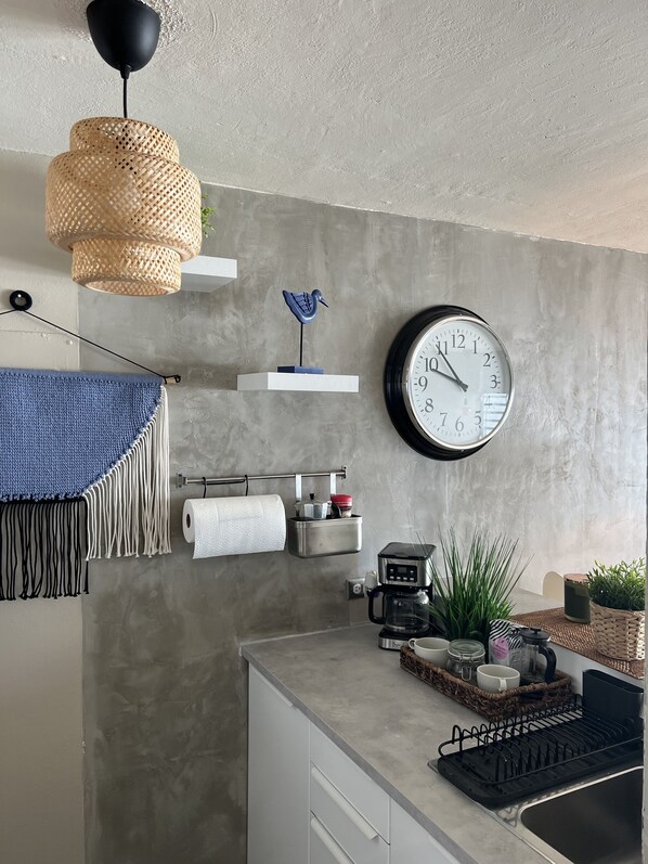A modern kitchen with a concrete backsplash, a hanging light fixture, a wall clock, and various kitchen appliances.
