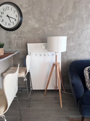 A modern room with a Tesla logo on the wall, a white chair, a blue sofa, and a floor lamp.