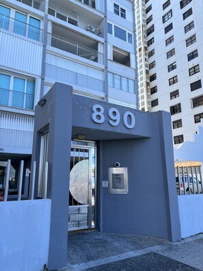 A modern building entrance with a large number '890' sign, a security keypad, and a metal gate.
