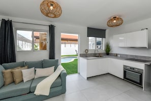 A modern kitchen with white cabinets, a built-in oven, and a grey countertop. There is a green sofa with a throw blanket and pillows in the living area. - Aruba Dushi Casa + Studio minutes to Eagle Beach ! (Noord)