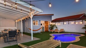 Un jardin avec une piscine, un espace salon extérieur et des guirlandes lumineuses.