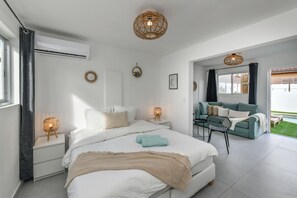 A modern bedroom with a large bed, bedside lamps, a sofa, and a view of the outdoors. - Aruba Dushi Casa + Studio minutes to Eagle Beach ! (Noord)