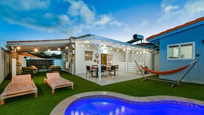 Un jardin avec une piscine, un espace salon extérieur et une terrasse couverte.