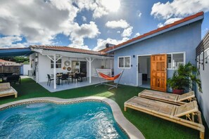 A backyard with a swimming pool, a covered patio, and a hammock.