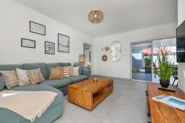 A modern living room with a grey sofa, wooden coffee table, and a large window offering a view of the outdoors.