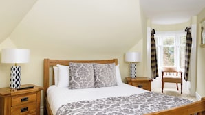 A neatly arranged bedroom with a bed, bedside tables, a chair, and a window with curtains. - 3 bedroom accommodation in Pitlochry (Pitlochry)