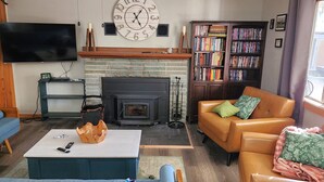 A living room with a fireplace, a television, a bookshelf, and a sofa. - Alpine Dog Friendly Cabin! (Alpine)