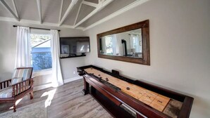 A room with a shuffleboard table, a television mounted on the wall, and a large mirror. - LaVerna! LaVerna! (Ocean Park)