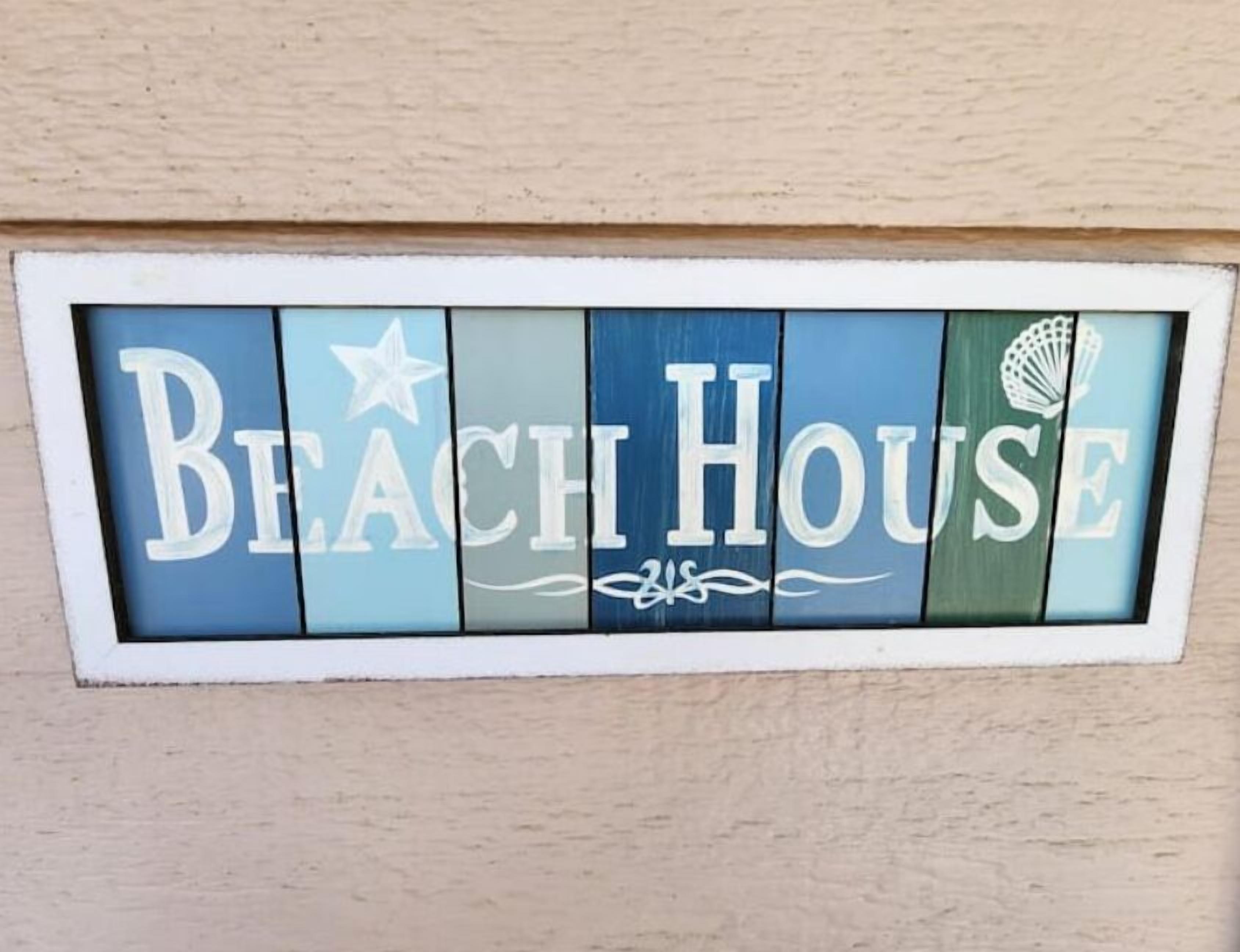 Een bord met de woorden 'Beach House' in een decoratief lettertype, met sterren en zeeschelpen als versiering.