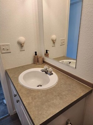 A bathroom with a white sink, beige countertop, and a mirror. There are two soap dispensers and a towel holder on the wall. - The Lynn Inn (Long Beach)