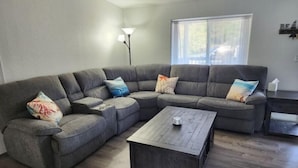 A living room with a sectional sofa, a coffee table, a floor lamp, and a window with blinds.