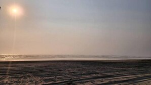 A beach with a clear sky and the sun low on the horizon.