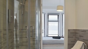 A modern bathroom with a glass shower enclosure, a visible bed with a white mattress, and a towel rack with a white towel. - A spacious town house, with lots of character. (Newquay)