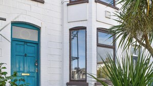 A white building with a blue door, windows, and a small plant in the foreground. - A spacious town house, with lots of character. (Newquay)