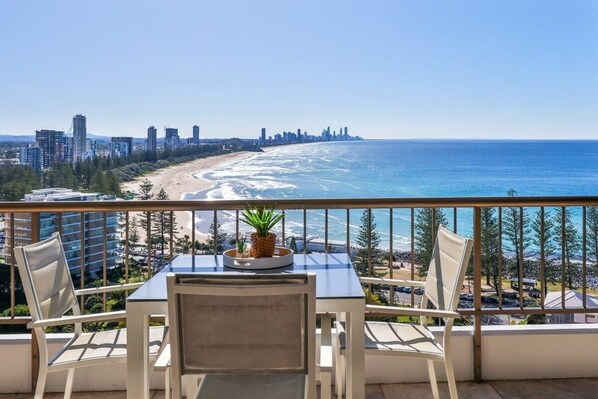 Un balcon avec une table et des chaises, offrant une vue sur la plage et le panorama de la ville.