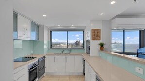 Une cuisine moderne avec des meubles blancs, une cuisinière noire et une grande fenêtre donnant sur la ville.